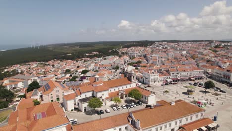 Aerial-ascending-Sanctuary-of-Nossa-Senhora-da-Nazaré-on-the-hilltop,-rooftops-on-Cityscape