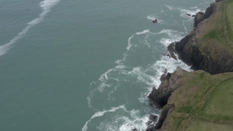 Quick-aerial-flyover-of-Irish-green-fields,-rocky-sea-cliffs-and-ocean