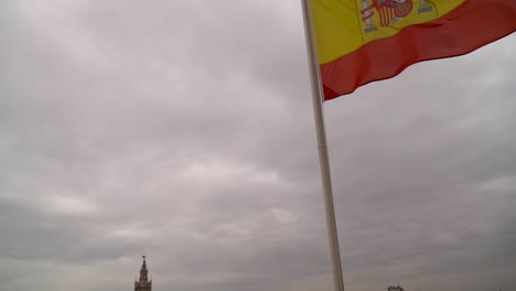 Reveal-of-Seville-cityscape-from-Spanish-flag-on-gray-cloudy-day