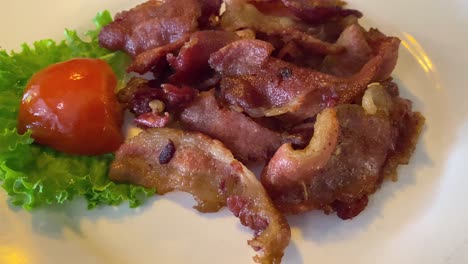 A-plate-of-fried-bacon-with-a-tomato-and-a-piece-of-lettuce