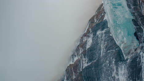 Vertical-4k-Time-lapse,-Glacier-and-Cliffs-Under-Thick-Fog-in-Cold-Mountain-Landscape,-Ice-and-Snow-on-High-Elevation,-global-warming-and-climate-change-concept