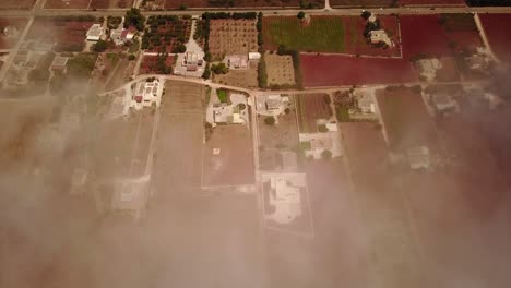 Static-shot-by-drone-of-a-colored-field-of-puglia,-clouds-are-between-the-drone-and-the-ground