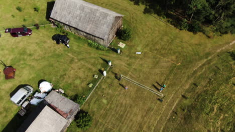Recreational-rural-homestead-with-people-playing-volleyball-on-green-grass-court,-aerial-orbit-view