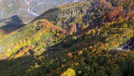 Mountain-road-snaking-through-dense-forest-with-colorful-foliage-in-Autumn,-in-Albanian-Alps