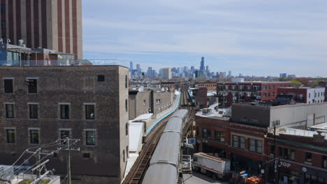 Long-gray-subway-slows-down-on-the-elevated-track-between-modern-and-traditional-buildings-to-enter-Damen-station-with-the-Chicago-skyline-in-the-background
