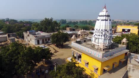 Pedestal-Aéreo-Arriba-Y-Panorámica-Del-Colorido-Templo-Hindú-De-La-Aldea-India-Rural-De-Khera-Kiran-En-Rajasthan,-India