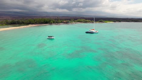 Big-island-Hawaiian-Anaehoomalu-Bay-boats-sailing-on-tropical-turquoise-ocean-landscape-aerial-flyover-shot