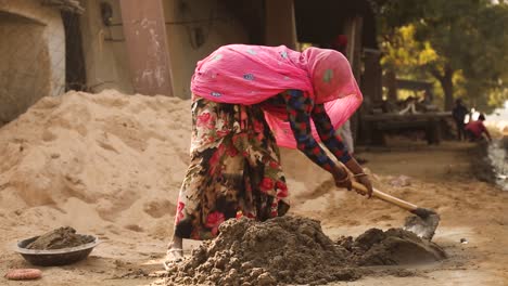 Unrecognizable-Indian-woman-with-head-covered-by-pink-veil-kneading-mortar-or-sand,-Tonk-district-in-Rajasthan