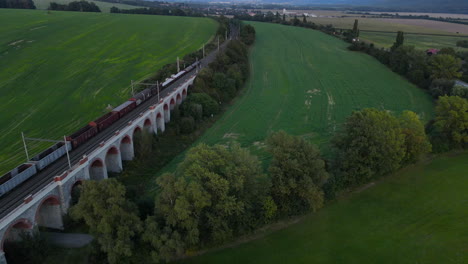 Luftaufnahme-Eines-Zugviadukts-Mit-Einem-Vorbeifahrenden-Zug-Und-Der-Umliegenden-Landschaft-Im-Hintergrund