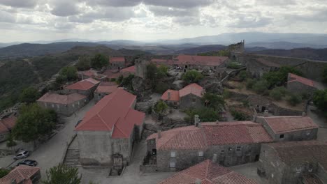 Drone-flying-over-roofs-of-granite-rural-houses-in-Sortelha-village-with-mountains-in-background,-Portugal