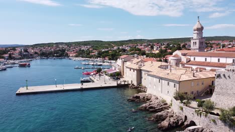 Krk-Village-at-Krk-Island,-Croatia---Aerial-Drone-View-of-the-Bay-with-Church,-Cathedral,-City-Walls,-Port,-Boats-and-Boulevard-at-the-Adriatic-Sea