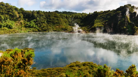 Panning-shot-of-boiling-volcanic-lake-in-National-Park-of-New-Zealand---Epic-green-mountains-and-clear-Lake-during-sunlight---Toxic-Sulfur-Steam-rising-up