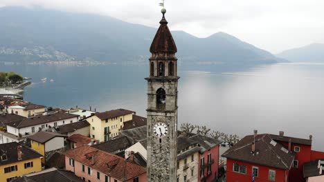 Aerial-flyover-around-the-belfry-tower-of-the-Chiesa-dei-Santi-Pietro-e-Paolo-church-and-over-the-rooftops-Ascona,-Switzerland-along-the-shores-of-Lago-Maggiore