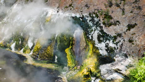 Panning-shot-of-boiling-water-geyser-with-tropical-colors-and-cliff-wall---Waimangu,New-Zealand