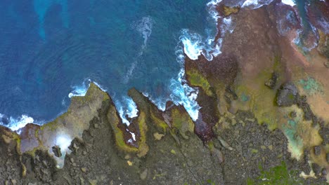 Schöne-Filmische-Aufnahme-Von-Wellen,-Die-An-Der-Felsigen-Küste-Krachen-Und-Tagsüber-Von-Einer-Drohne-Aus-Ein-Schaummuster-Auf-Dem-Riff-Erzeugen