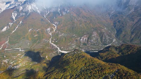 Fliegen-über-Die-Wolken-über-Ein-Wunderschönes-Tal,-Das-Mit-Buntem-Herbstlaub-Bedeckt-Ist,-In-Den-Alpen-Albaniens