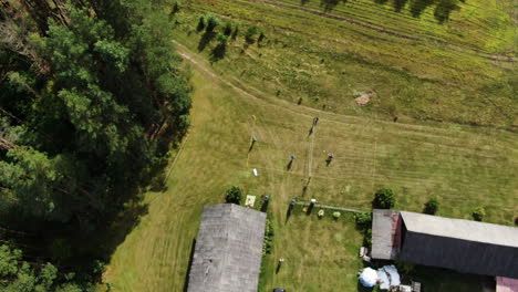 Group-of-people-plays-volleyball-in-old-recreational-farmstead-with-green-grass,-aerial-orbit-view
