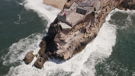 Ocean-waves-crashing-on-Nazaré-lighthouse-cliff,-Portugal