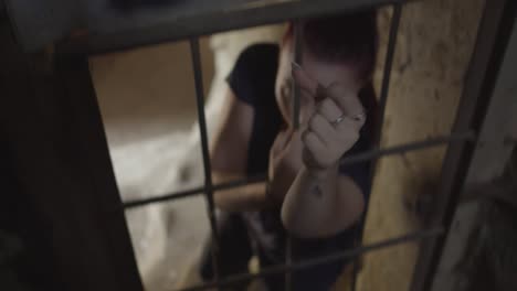 A-young-woman-stretches-out-her-hand-through-the-bars-trapped-in-an-old,-abandoned-building