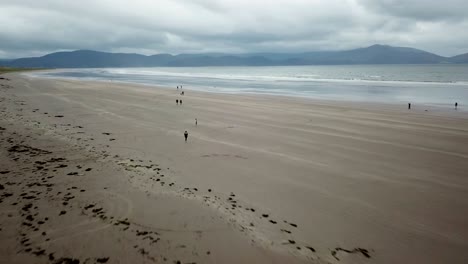 People-walk-on-wide-Irish-sandy-beach,-Dingle-Peninsula