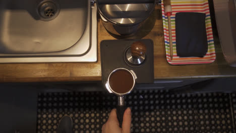 Barista-tamping-coffee-grinds-at-a-coffee-machine-inside-a-small-cafe-bar