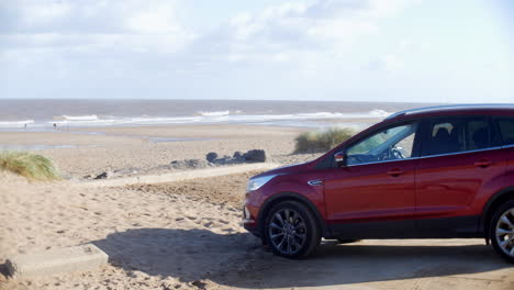 Red-SUV-car-parked-at-the-beach-on-the-sand-next-to-the-ocean