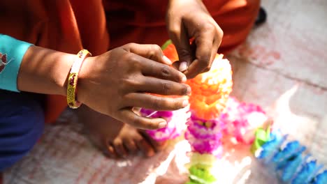 Manos-De-Mujer-Haciendo-Un-Collar-Indio-Tradicional-Con-Flores-De-Tela-En-La-Aldea-De-Noondpura,-Rajasthan
