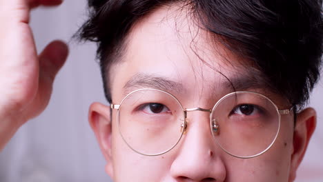 Close-up-Asian-man-with-glasses-and-healthy-good-hair-looking-to-the-camera-and-spoiling-himself-by-tidying-his-hair