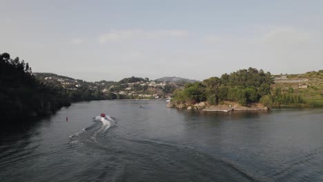 Aerial-tracking-of-red-motorboat-sailing-on-river-waters-of-Ilha-dos-Amores-love-Island,-Castelo-de-Paiva-in-Portugal