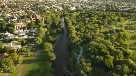 Aerial-flyover-beautiful-Suquia-River-surrounded-by-green-area-in-Cordoba-City-in-Argentina-during-summer