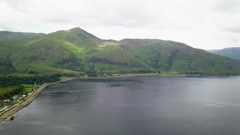 Aerial-drone-forward-view-of-Sgurr-Dhomnhuill-mountain-and-fishing-traps-on-lake-water-surface