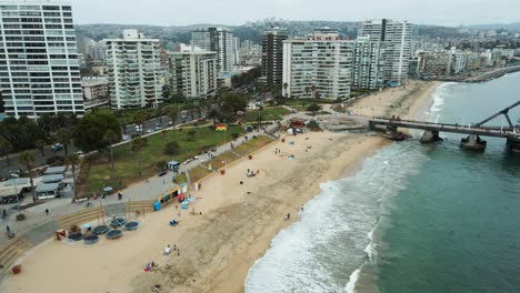 Aerial-view-passing-above-El-Sol-beach-at-Viña-del-Mar-city-on-a-cloudy-day