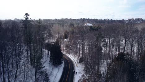 Aerial-fly-over-of-winding-road-through-winter-forest-landscape