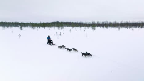 Two-People-Enjoying-Husky-Ride-Winter-Adventure-In-A-Snowy-Field-In-Muonio,-Lapland,-Finland