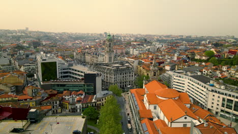 Beautiful-building-with-orange-roof-and-high-church-tower-on-a-large-square-full-of-green-trees-in-the-city-center-of-the-portuguese-city-of-Porto-on-a-cloudy-day