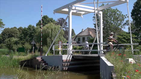 Adult-Men-Biking-And-Crossing-Bridge-Over-Stream-In-Reeuwijkse-Plassen-On-A-Sunny-Day-In-Netherlands