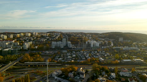 Aerial-trucking-shot-showing-Cityscape-of-Gdynia-during-sunrise-and-blue-Baltic-Sea-in-backdrop---Housing-area-district-with-high-rise-building-complex-during-sunny-autumn-day-in-Poland,Europe