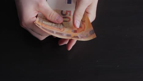 Pagando-Billetes-De-50-Euros,-Manos-Contando-Dinero,-Fondo-Negro-Oscuro,-Cierre-Estático