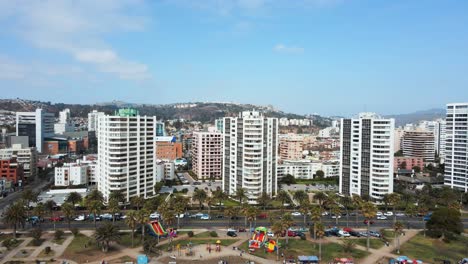 Aerial-orbit-of-Viña-del-Mar-buildings-and-touristic-apartments-near-sea-shore-and-avenue-surrounded-by-palm-trees-at-daytime,-Chile