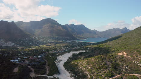 Magnificent-View-Of-Sandy-Bay-Beach-With-Houtbay-Harbor-Town-In-Background-In-South-Africa---aerial-shot