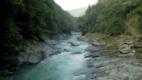 Antena-De-Seguimiento-Hacia-Atrás-Sobre-El-Río-Azul-verde-Que-Fluye-A-Través-De-Las-Montañas-En-La-Isla-De-Shikoku,-Japón