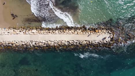 Old-ruined-pier-on-pebbly-beach-with-tourists