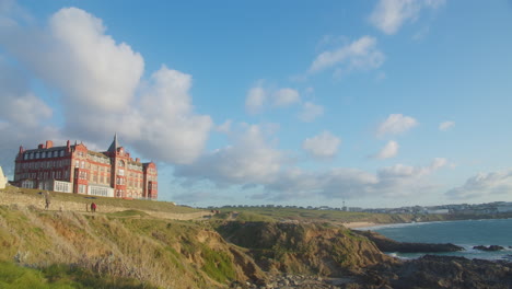 Headland-Hotel-on-Top-of-a-Hill-Overlooking-the-Fistral-Beach-with-Tourists-Walking-Along-the-Footpath-Going-to-the-Beach-in-Cornwall,-England---Timelapse