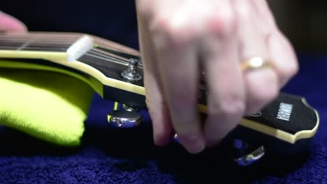 Restringing-and-cleaning-a-beautiful-black-single-cutaway-accoustic-guitar---close-up-of-loosening-the-strings-at-the-headstock