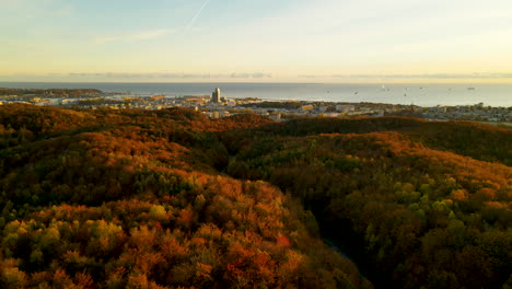 Luftdrohnenflug-über-Hügel-Mit-Bunten-Herbstwaldbäumen-In-Richtung-Gdynia-Stadt,-Ostsee-Im-Hintergrund-Bei-Goldenem-Sonnenuntergang