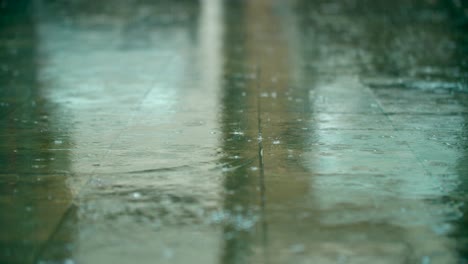 Rainfall-drops-and-splashes-hit-the-pavement-tile-path-sidewalk