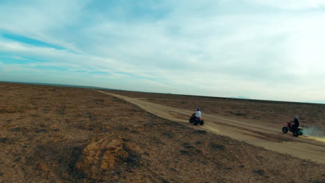 Riding-three-wheeler-motorized-trike-all-terrain-vehicles-along-a-Mojave-Desert-dirt-trail---slow-motion