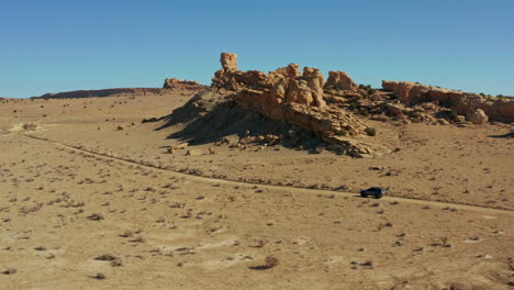 Scenic-aerial-following-car-on-desert-dirt-road-with-hoodoo-rock-formations