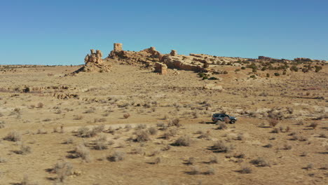 Aerial-tracking-with-4x4-car-on-desert-dirt-road-with-rock-formations-behind