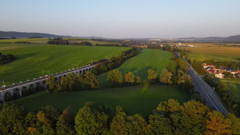 Aerial-view-of-a-train-viaduct-with-a-highway-and-the-countryside-and-the-city-lying-in-the-background